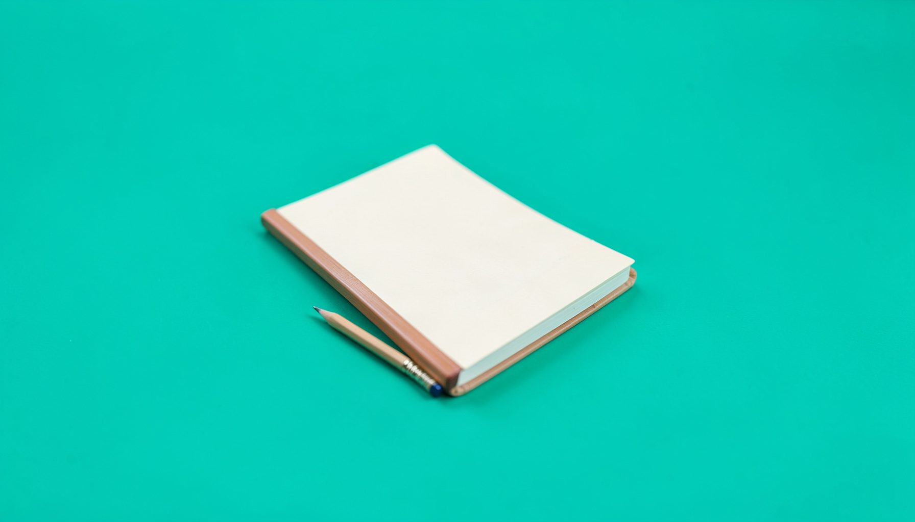 Açık tonlarda, yumuşak ışıkla aydınlatılmış küçük bir defter ve kurşun kalem.